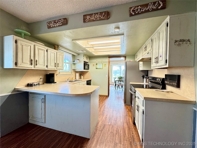 kitchen with stainless steel electric stove, wood-type flooring, sink, white cabinets, and a textured ceiling