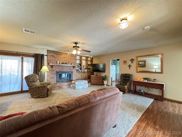 living room with a brick fireplace, wood-type flooring, a textured ceiling, and ceiling fan