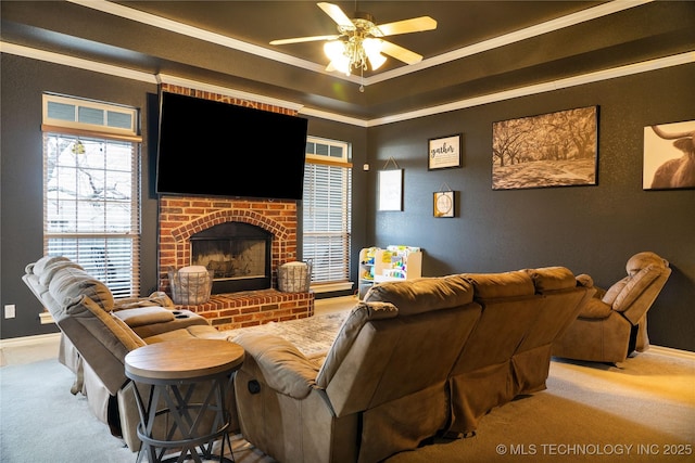 living room featuring a fireplace, carpet flooring, ceiling fan, a raised ceiling, and crown molding