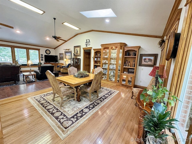 dining space featuring crown molding, ceiling fan, vaulted ceiling with skylight, and hardwood / wood-style floors