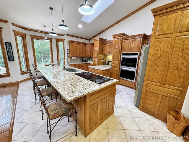 kitchen with lofted ceiling with skylight, decorative light fixtures, sink, stainless steel appliances, and a spacious island