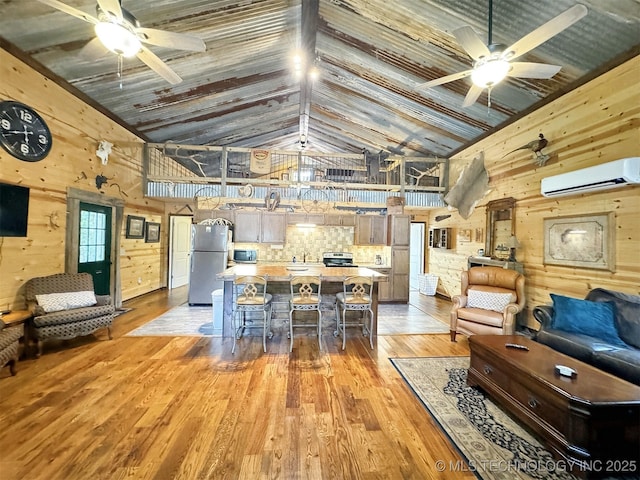 living room with high vaulted ceiling, a wall mounted air conditioner, ceiling fan, and light hardwood / wood-style flooring