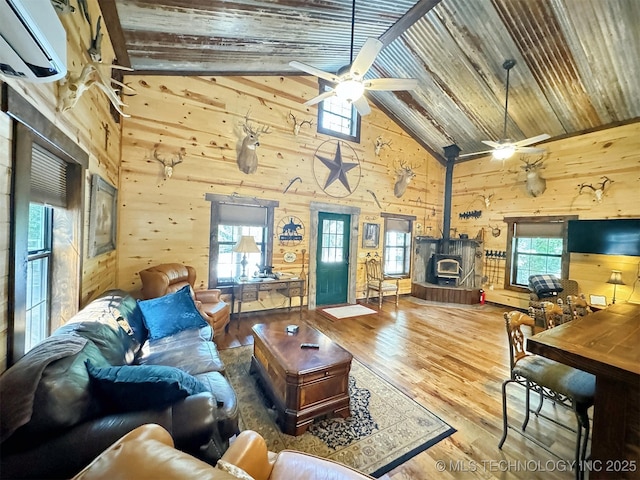 living room featuring a wall mounted air conditioner, high vaulted ceiling, a wood stove, wooden walls, and hardwood / wood-style flooring