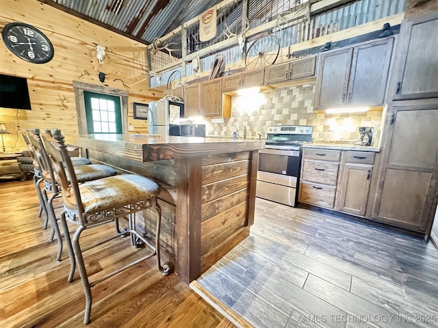 kitchen featuring hardwood / wood-style flooring, wood walls, stainless steel appliances, and a high ceiling