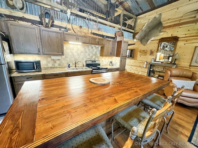 kitchen with sink, a breakfast bar area, appliances with stainless steel finishes, backsplash, and hardwood / wood-style floors