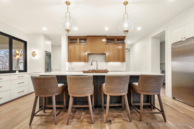 kitchen featuring white cabinetry, built in refrigerator, a kitchen island with sink, and hanging light fixtures