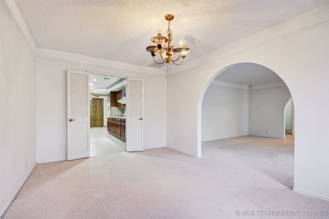 carpeted spare room with ornamental molding, a textured ceiling, and an inviting chandelier