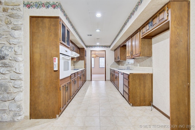 kitchen with sink, dishwasher, backsplash, a notable chandelier, and oven