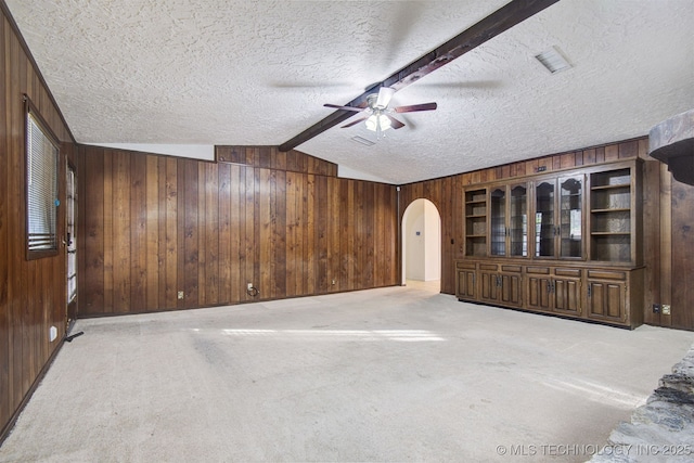 interior space with lofted ceiling with beams, wooden walls, light carpet, and a textured ceiling