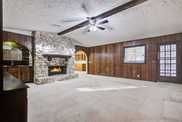 unfurnished living room with sink, carpet flooring, a fireplace, lofted ceiling with beams, and a textured ceiling