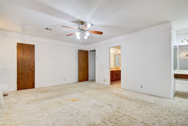 unfurnished bedroom featuring ensuite bath, light colored carpet, ceiling fan, and a textured ceiling