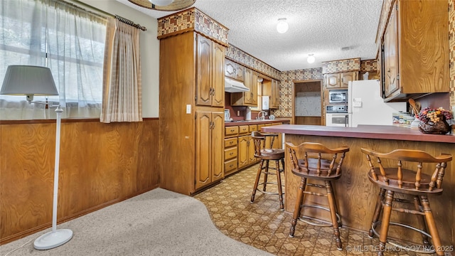 kitchen with a breakfast bar area, wood walls, a textured ceiling, kitchen peninsula, and white appliances