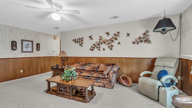 living room with ceiling fan, light carpet, a textured ceiling, and wood walls