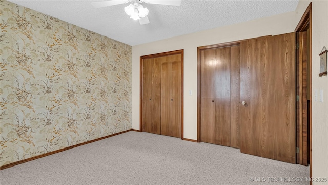 unfurnished bedroom with two closets, light colored carpet, ceiling fan, and a textured ceiling