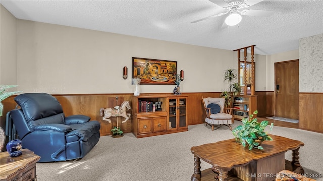 living room featuring ceiling fan, carpet flooring, a textured ceiling, and wood walls