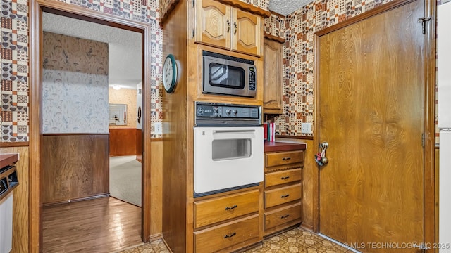 kitchen with stainless steel microwave, wooden walls, oven, and a textured ceiling