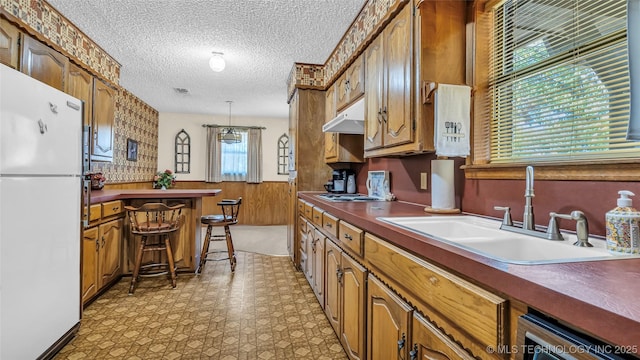 kitchen with a kitchen bar, sink, wood walls, white refrigerator, and pendant lighting