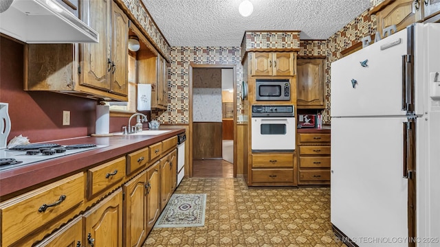 kitchen featuring sink, white appliances, a textured ceiling, custom exhaust hood, and wood walls