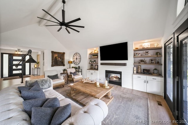 living room with built in features, high vaulted ceiling, hardwood / wood-style flooring, ceiling fan, and beam ceiling