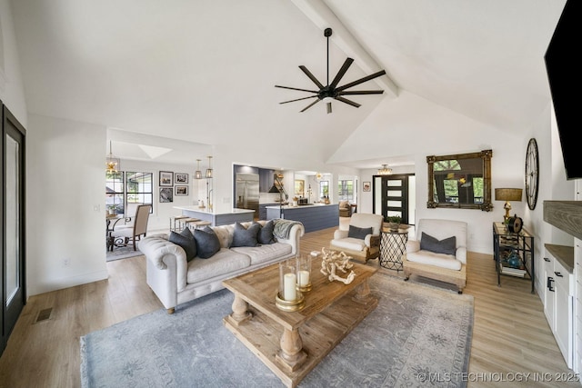 living room with high vaulted ceiling, ceiling fan with notable chandelier, light hardwood / wood-style floors, and beamed ceiling