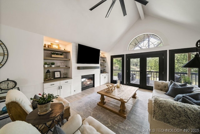 living room with beam ceiling, high vaulted ceiling, a large fireplace, built in shelves, and french doors