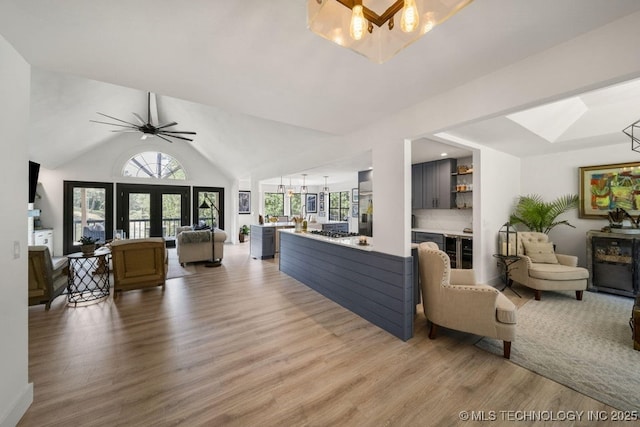 living room with ceiling fan with notable chandelier, vaulted ceiling, french doors, and light wood-type flooring