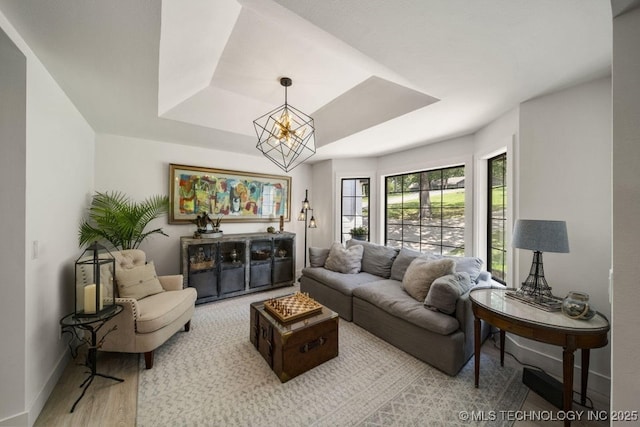 living room with a notable chandelier, a tray ceiling, and light wood-type flooring