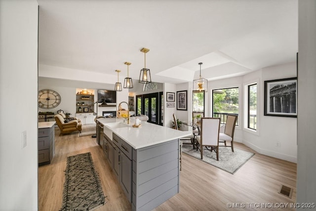 kitchen featuring gray cabinetry, a center island, light wood-type flooring, a raised ceiling, and pendant lighting