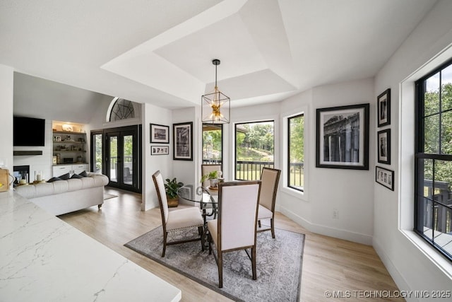 dining space featuring french doors, a chandelier, a raised ceiling, built in shelves, and light hardwood / wood-style flooring