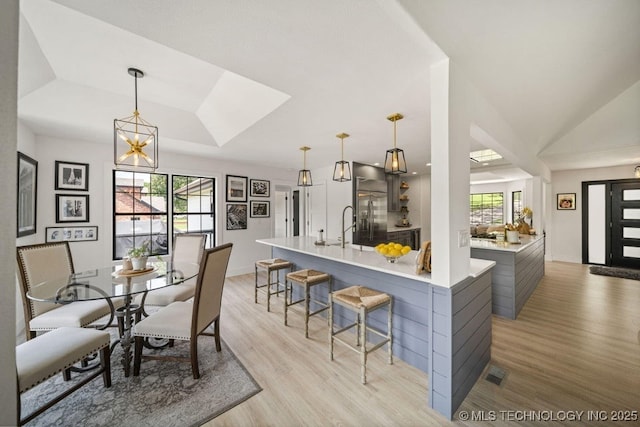 kitchen featuring hanging light fixtures, light hardwood / wood-style flooring, a breakfast bar, and a raised ceiling