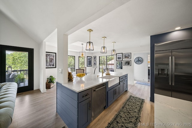 kitchen with sink, hanging light fixtures, light wood-type flooring, appliances with stainless steel finishes, and light stone countertops