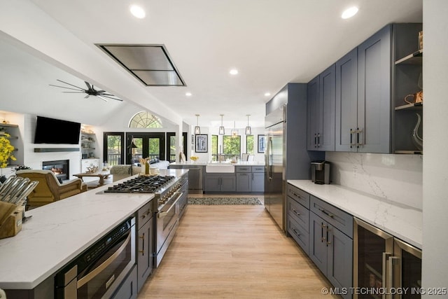 kitchen featuring appliances with stainless steel finishes, light stone countertops, decorative backsplash, beverage cooler, and light wood-type flooring