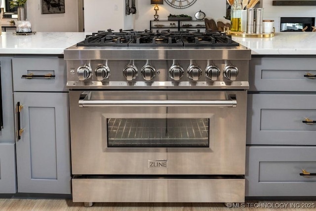 interior details featuring gray cabinetry, light stone counters, and high end stainless steel range