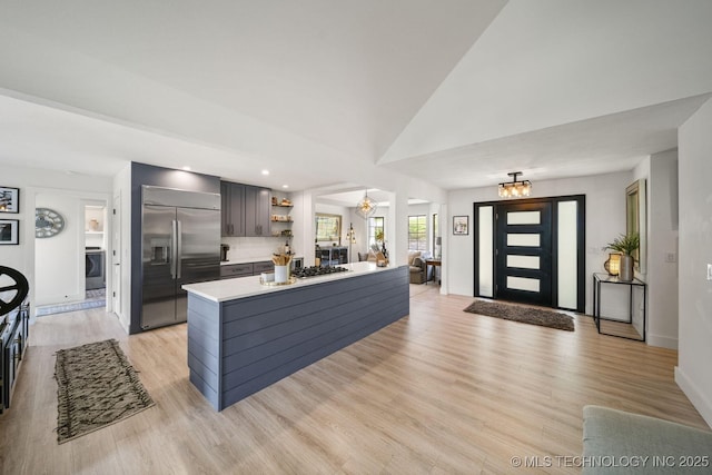 kitchen featuring an inviting chandelier, light wood-type flooring, appliances with stainless steel finishes, a kitchen island, and decorative backsplash