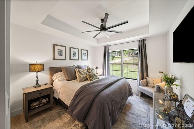 bedroom featuring hardwood / wood-style floors, a raised ceiling, and ceiling fan