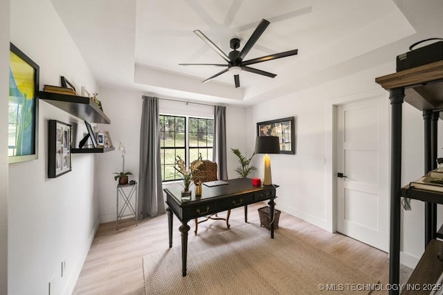 office space featuring a raised ceiling, ceiling fan, and light hardwood / wood-style flooring