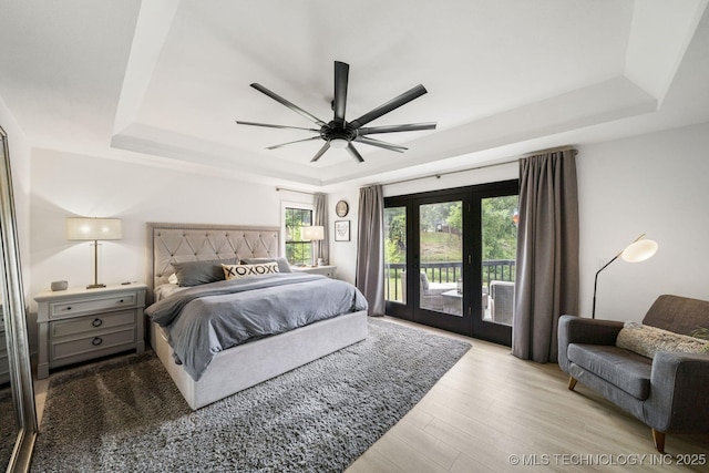 bedroom featuring light hardwood / wood-style flooring, access to outside, ceiling fan, and a tray ceiling