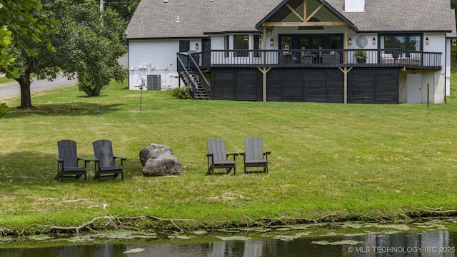 rear view of property with a deck with water view, a yard, and central AC