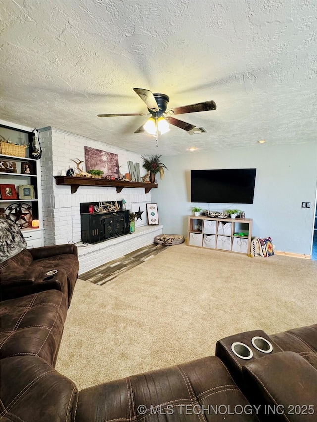 living room with ceiling fan, carpet floors, a fireplace, and a textured ceiling