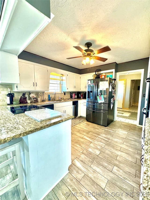 kitchen with stainless steel refrigerator with ice dispenser, white cabinetry, a textured ceiling, kitchen peninsula, and light stone countertops