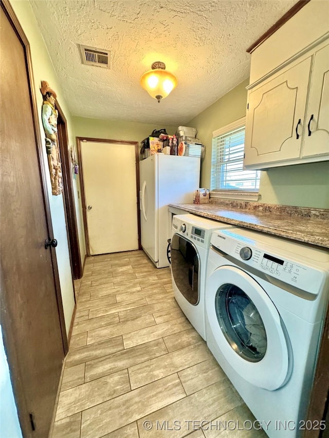 laundry area with cabinets, washing machine and clothes dryer, and a textured ceiling