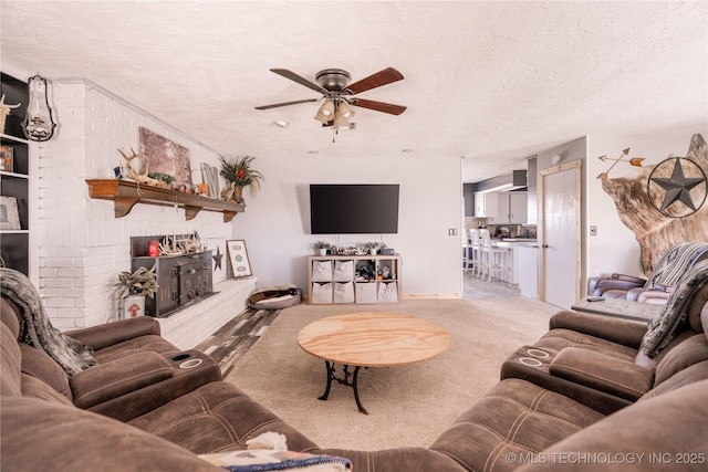 living room with a fireplace with raised hearth, a ceiling fan, carpet floors, and a textured ceiling