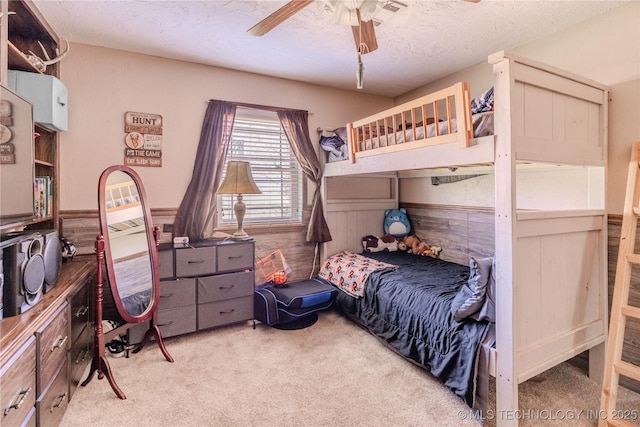 carpeted bedroom featuring a textured ceiling, ceiling fan, wainscoting, and wood walls