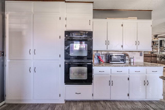 kitchen featuring ceiling fan, light stone counters, wood finished floors, white cabinetry, and dobule oven black