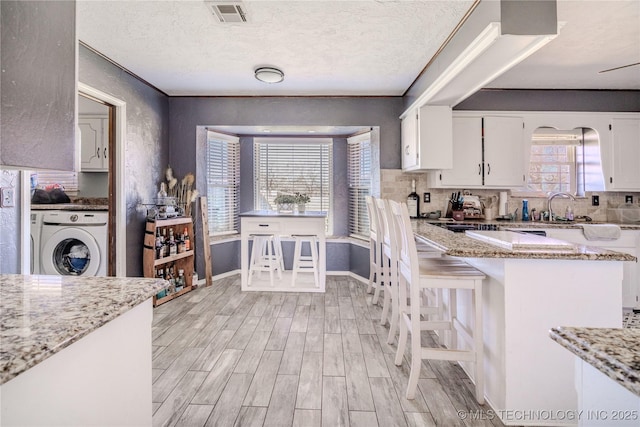 kitchen with light wood-type flooring, visible vents, light stone counters, washer / clothes dryer, and white cabinetry