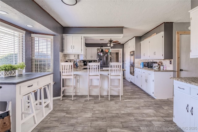 kitchen with stainless steel refrigerator with ice dispenser, a ceiling fan, a kitchen breakfast bar, white cabinets, and decorative backsplash