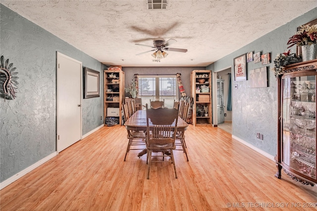 dining space featuring light wood finished floors, visible vents, a textured ceiling, and a textured wall