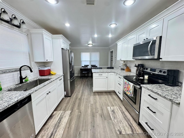 kitchen with sink, white cabinetry, stainless steel appliances, light stone countertops, and light hardwood / wood-style floors