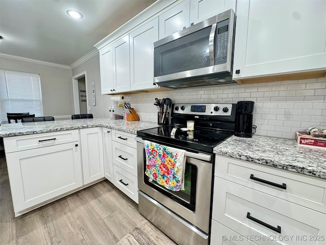 kitchen featuring ornamental molding, appliances with stainless steel finishes, kitchen peninsula, white cabinets, and backsplash