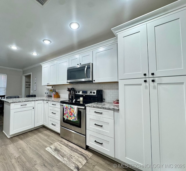 kitchen with tasteful backsplash, appliances with stainless steel finishes, kitchen peninsula, and white cabinets